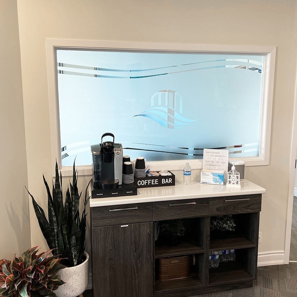 The coffee bar at River Family Dentistry, under the etched glass panel carrying their logo